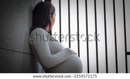 Portrait of mature pregnant woman at home looking outside the fence. Young pregnant woman standing by fence at home and thinking about the future.