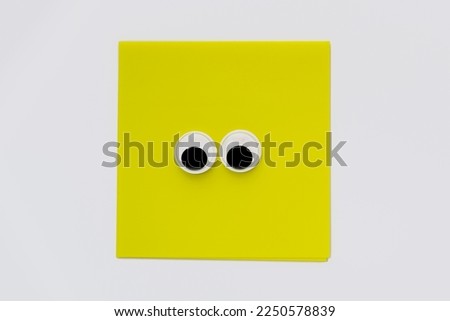 Pair of cute googly eyes on yellow square note pad isolated on a white background