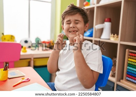 Adorable hispanic boy preschool student sitting on table crossing fingers at kindergarten