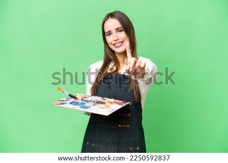 Young artist woman holding a palette over isolated chroma key background showing and lifting a finger