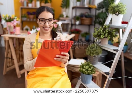Young arab woman florist writing on document sitting on chair at flower shop