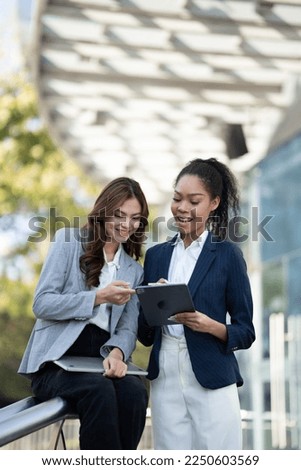 Two Asian businesswomen discussing business information while standing outside the office.