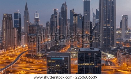 Panorama of Dubai Financial Center district with tall skyscrapers with illumination night to day transition . Aerial view to towers along busy highway before sunrise