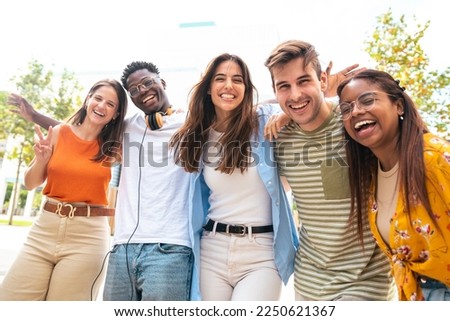 Low angle view of a happy group of multiracial friends looking at camera, enjoying outdoors. Multiethnic cheerful young people