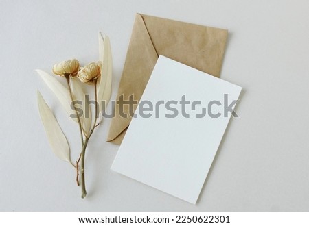 Greeting card mockup, envelope and dry eucalyptus twigs and roses on beige background top view flatlay. Card mockup with copy space.