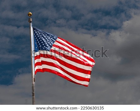 Flag of the United States of America waving on a background of fluffy white clouds in a blue sky.