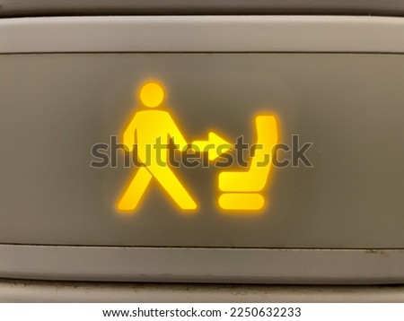 A close up view of an illuminated "return to seat" icon inside an airplane lavatory. This sign comes on whenever the seatbelt sign is activated during flight