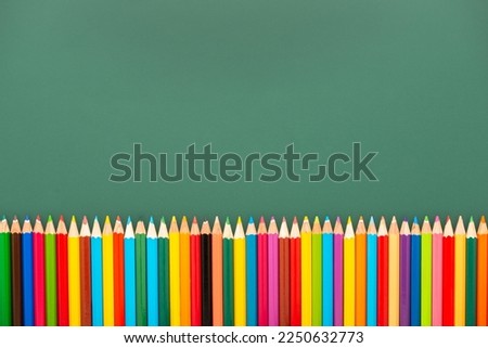 multicolored pencils is on green chalkboard background, top view, copy space, back to school concept.