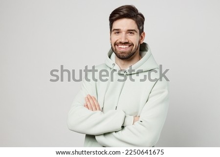 Young confident smiling happy cheerful unshaven caucasian man wear mint hoody look camera hold hands crossed folded isolated on plain solid white background studio portrait. People lifestyle concept