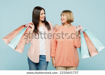 Cheerful fun elder mom with young adult daughter two women wear casual clothes hold paper package bags after shopping isolated on plain light pastel blue background. Black Friday sale buy day concept