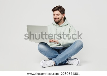Full body smiling happy programmer smart young caucasian IT man wear mint hoody hold use work on laptop pc computer isolated on plain solid white background studio portrait. People lifestyle concept