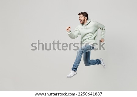 Full body side view overjoyed cheerful happy excited young caucasian man wear mint hoody jump high run fast hurry up isolated on plain solid white background studio portrait. People lifestyle concept Royalty-Free Stock Photo #2250641887