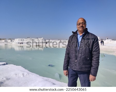 Picture of a man standing on a hill covered with snow and river in background shot during daylight. White snowy mountain hills, nature, landscape in winter. Trekking and hiking. Adventure love