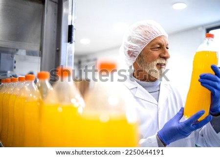 Factory supervisor controlling production of bottled orange juice for the market. Royalty-Free Stock Photo #2250644191