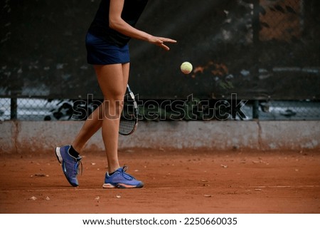 close-up view of legs of woman tennis player with tennis racket which catch ball with her hand. Tennis player prepares to serve during the match.