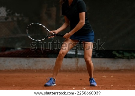 Close-up view of body and atletic legs of female tennis player holding racket and preparing to hitting. Outdoor tennis practice.