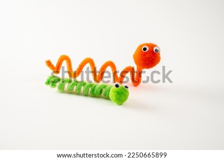 googly eyed pom pom pipe cleaner orange wriggly worm green caterpillar funny character childs toy hand made isolated on a white background
