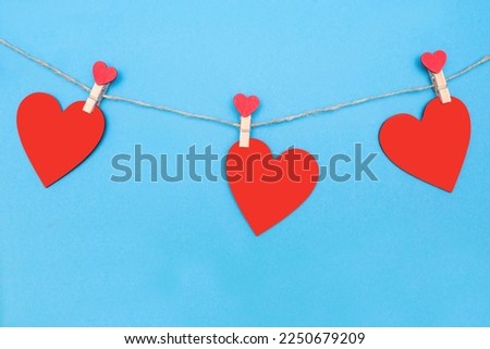 Three red hearts are attached to a rope with clothespins on a blue background. Beautiful decor in the form of hearts or decoration for Valentine's Day. Red wooden hearts on blue paper background