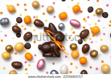 Happy Easter concept. Delicious traditional chocolate Easter bunny, eggs, sweets, almonds, sugar stars on white table background. Preparation for holiday. Simple minimalism flat lay, top view