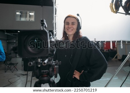 The director of photography is a woman with a video camera on the set. A professional videographer at work on the filming of a movie, commercial or TV series. Filming process indoors, studio Royalty-Free Stock Photo #2250701219