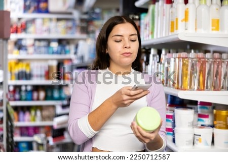 Woman photographing skin or hair care product with smartphone while standing in beauty shop