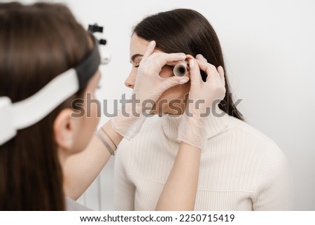 ENT doctor with ear funnel. Otoscopy. Otolaryngologist is looking through otoscope the ears of woman. Treatment ear pain Royalty-Free Stock Photo #2250715419