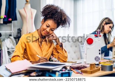 Portrait of young african american woman and young girl fashion designer stylish sitting and working with color samples.Attractive two designer girl work with colorful fabrics at fashion studio
