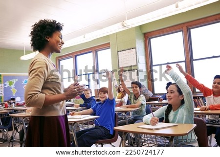 School, teacher and children raise their hands to ask or answer an academic question for learning. Diversity, education and primary school kids speaking to their woman educator in the classroom. Royalty-Free Stock Photo #2250724177