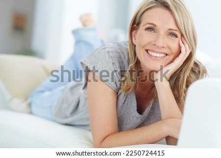 Portrait of mature woman lying on sofa in living room, happiness and relaxing in comfort at home. Smile, lazy weekend time and happy woman in peace chilling on comfortable couch in apartment on break Royalty-Free Stock Photo #2250724415