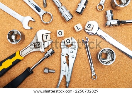 Top view of wrenches, screwdrivers and pliers near cubes with TOOLS sign on cork table