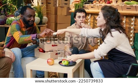 Consumers having fun with local stall holders at food testing festival, trying out locally grown fruits and veggies. Smiling clients and business owners eating produce and drinking organic wine. Royalty-Free Stock Photo #2250739833