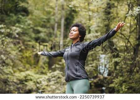 Black woman standing in nature with arms outstretched and enjoying in fresh air. Royalty-Free Stock Photo #2250739937