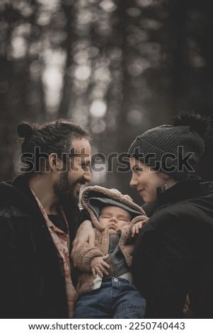 New born family photo shoot in the fall by the woods. Mother and father looking lovingly into each other’s eyes as baby sleeps.