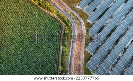 Fly over Solar cells farm beside nature green farm around large industrial factory area. Solar farms are generating renewable energy for the industry.  Royalty-Free Stock Photo #2250777765