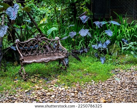 Empty old lonely vintage iron bench seat, chair at the desolate yard on the green forest background.