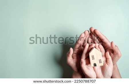 Hands holding wooden house, family home, homeless housing, mortgage crisis and home protecting insurance, international day of families, foster home care, family day care, stay home concept Royalty-Free Stock Photo #2250788707
