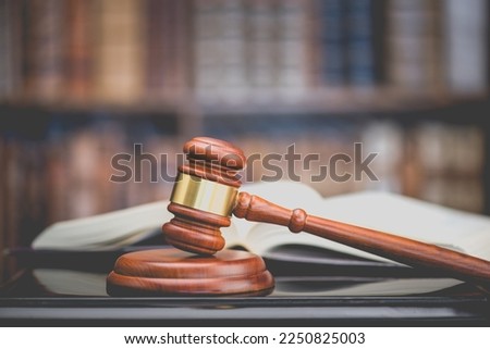 Legal office of lawyers, justice and law concept : Judge's gavel or hammer and base used by a judge person on a desk in a courtroom with blurred books and a bookshelf or bookcase in the background. Royalty-Free Stock Photo #2250825003