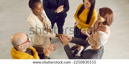 Group of cheerful positive diverse multiethnic people meeting and getting acquainted at casual business event. Young black woman feeling at ease and exchanging handshake with senior man. High angle