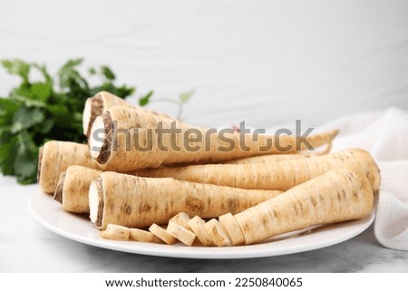 Plate with whole and cut parsley roots on white table, closeup Royalty-Free Stock Photo #2250840065