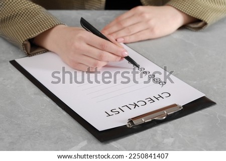 Woman filling Checklist at grey marble table, closeup