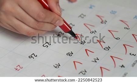 Blurred calendar page. Close-up female hand cross out days in calendar. Red circle marked with pen on a calendar sheet
