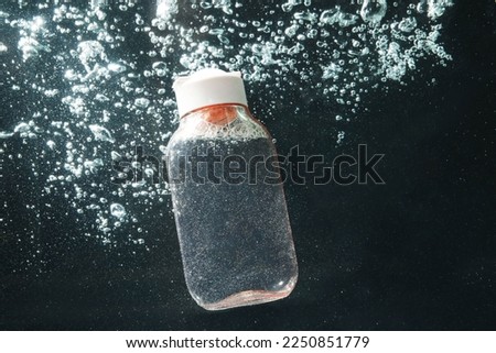 Bottle of micellar water in liquid with bubbles on black background