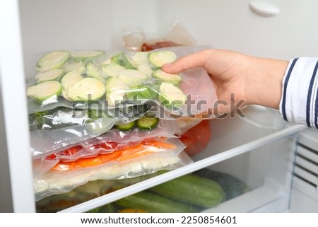 Woman putting vacuum bags with vegetables into fridge, closeup. Food storage Royalty-Free Stock Photo #2250854601