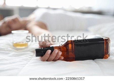 Woman is lying in bed dead drunk holding almost empty bottle of booze Royalty-Free Stock Photo #2250861317
