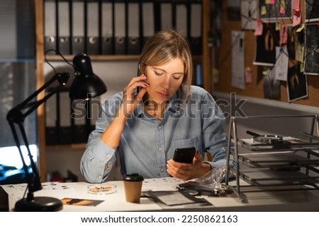 Detective working at desk in her office looking at cellphone. Copy space