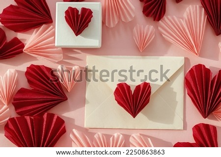 Happy Valentine's day! Stylish envelope with pink and red hearts and gift flat lay on pink paper background. Modern valentine card with heart cutouts. Love letter. Creative composition