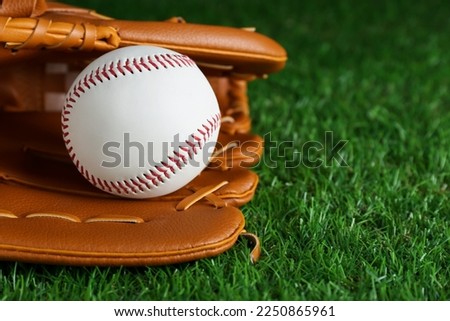Catcher's mitt and baseball ball on green grass, closeup with space for text. Sports game