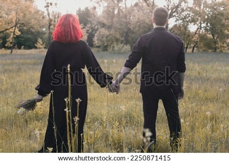 Couple in dark holding hands among meadow scenic photography. Picture of woman and man with nature on background. High quality wallpaper. Photo concept for ads, travel blog, magazine, article