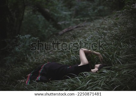 Lying in dark forest thick grass scenic photography. Picture of young sleepy woman with deep woodland on background. High quality wallpaper. Photo concept for ads, travel blog, magazine, article