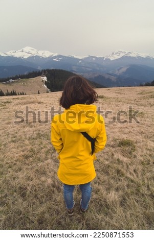 Close up woman in yellow coat looking at snowy mountain peaks concept photo. Back view photography with landscape on background. High quality picture for wallpaper, travel blog, magazine, article
